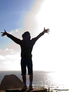 Happy, Young Boy Looking Out Over the Ocean and Bright Sun from a Cliff Edge